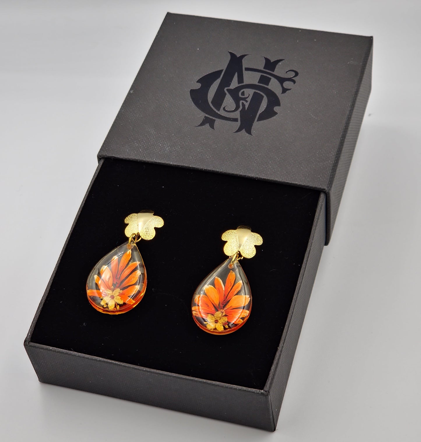 Aretes artesanales de resina con una flor naranja encapsulada, hechos en el Eje Cafetero, Colombia, con baño de oro para un acabado brillante y duradero, ideales para lucir elegancia y sofisticación en joyería fina.