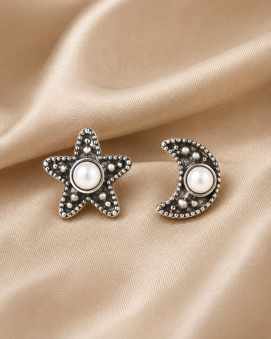Handcrafted celestial star and moon stud earrings in oxidized Mexican silver with pearl centers. A refined, distinctive mismatched design.