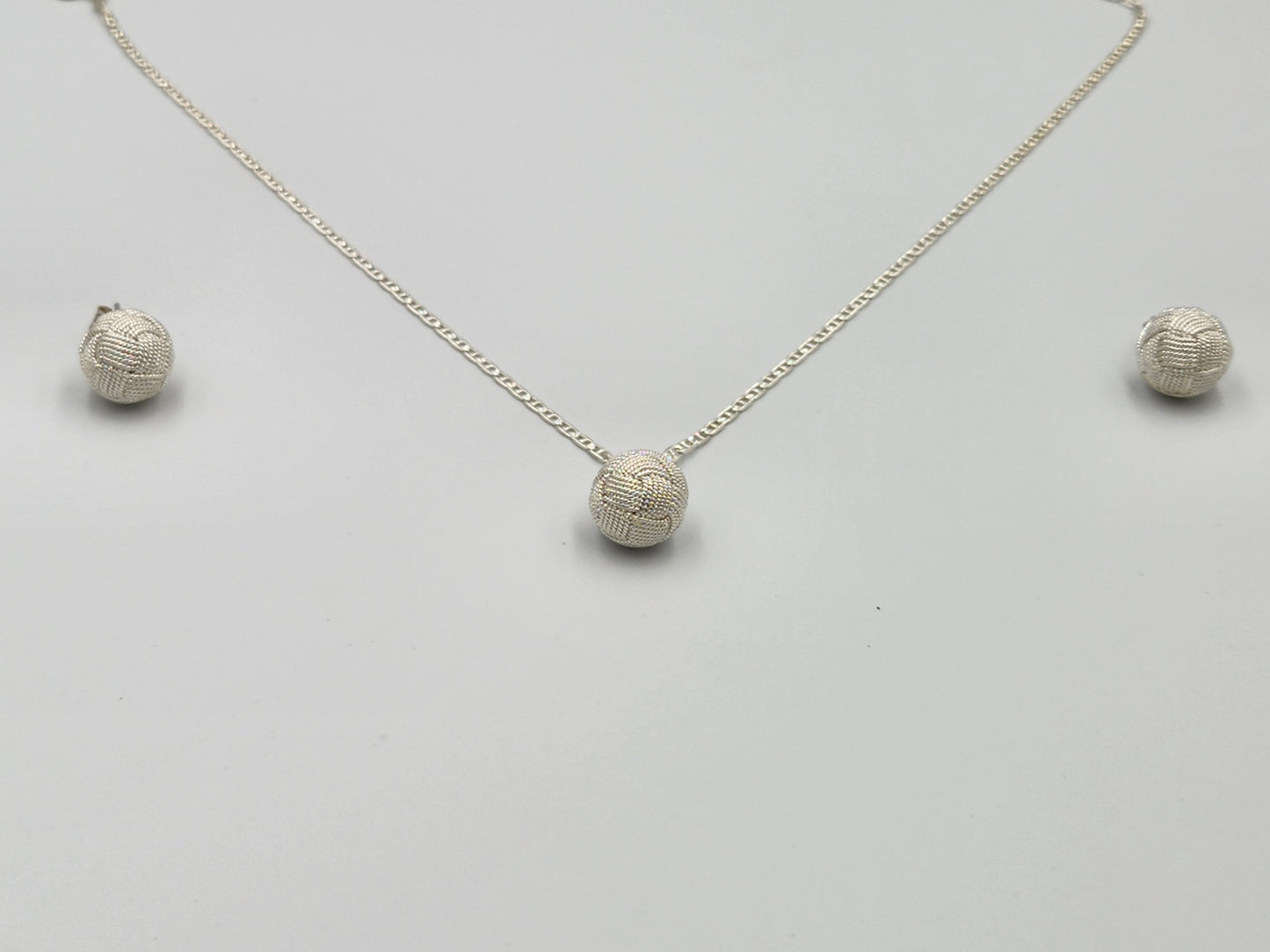 Profesional y elegante en fondo blanco luciendo un juego de joyería en plata 950 con diseño de filigrana y el nudo tradicional de Santa Fe de Antioquia, ideal para destacar en el mercado de Estados Unidos