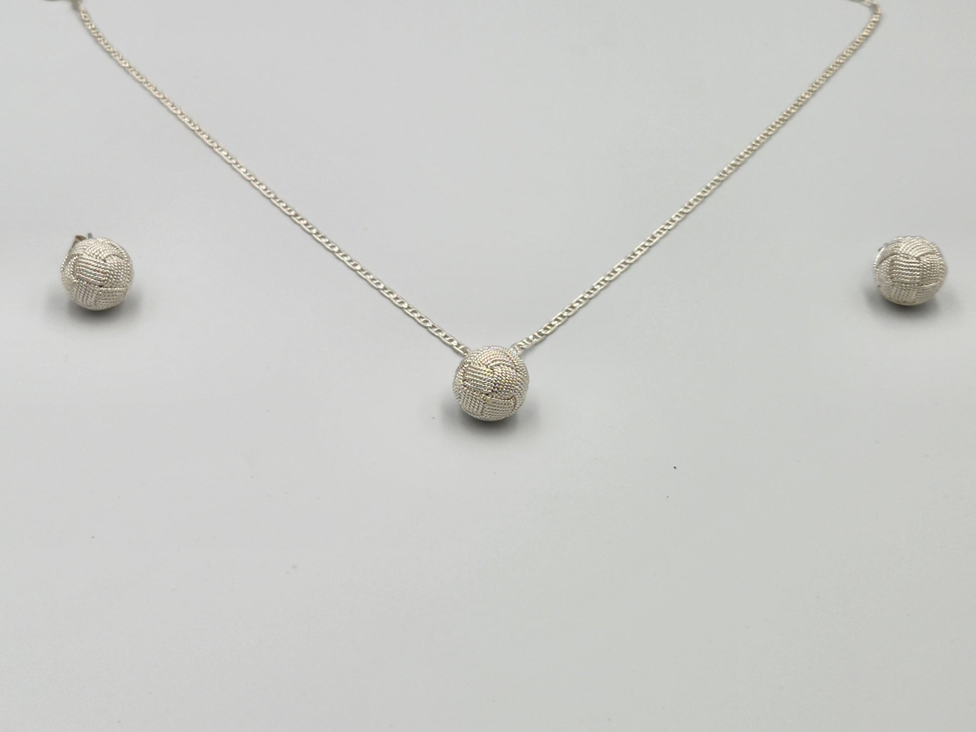 Profesional y elegante en fondo blanco luciendo un juego de joyería en plata 950 con diseño de filigrana y el nudo tradicional de Santa Fe de Antioquia, ideal para destacar en el mercado de Estados Unidos